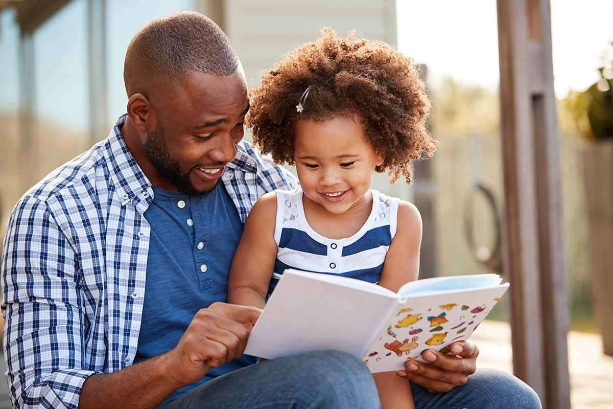 Caregiver is reading to his child enjoying a book from the Berkeley Public Library.